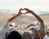 Para, które właśnie wzięło ślub, leży na plaży, tworząc serce dłońmi. Idealne miejsce na podróż poślubną.