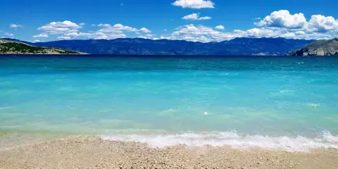 Idealne miejsce, gdzie lecieć w czerwcu: turkusowe morze, kamienista plaża i góry w tle. Idealny widok na wakacje.