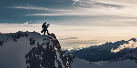 Sylwester w Alpach: snowboardzista na szczycie góry, gotowy na zjazd. W tle majestatyczne, ośnieżone szczyty i dramatyczne chmury.