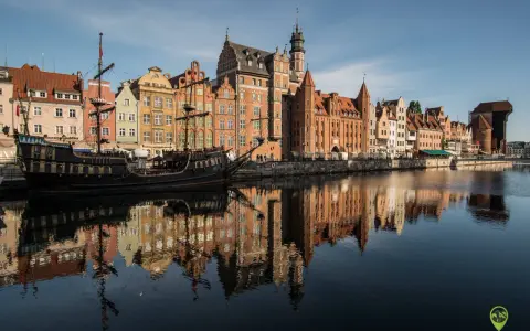 Gdańsk atrakcje: zabytkowy żaglowiec cumuje przy Motławie, w tle kolorowe kamienice i Żuraw. Odbicia budynków w wodzie.