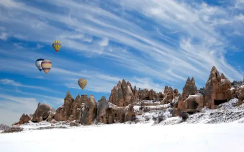 Balony unoszą się nad ośnieżonymi formacjami skalnymi w Kapadocji. Czy w Turcji pada śnieg? Tak, zimą krajobraz potrafi być bajkowy.