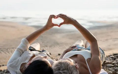 Para, które właśnie wzięło ślub, leży na plaży, tworząc serce dłońmi. Idealne miejsce na podróż poślubną.