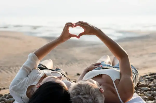Para, które właśnie wzięło ślub, leży na plaży, tworząc serce dłońmi. Idealne miejsce na podróż poślubną.