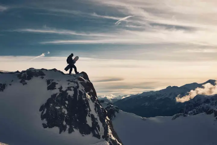Sylwester w Alpach: snowboardzista na szczycie góry, gotowy na zjazd. W tle majestatyczne, ośnieżone szczyty i dramatyczne chmury.